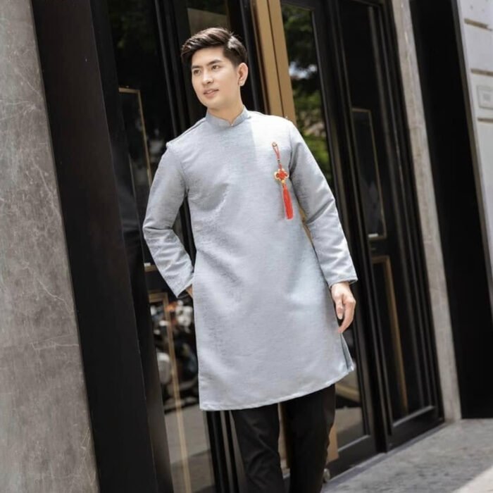 Áo Dài Cách Tân Nam Kèm Dây Tua Rua Xám mang hơi thở hiện đại, kết hợp giữa sự lịch lãm, mạnh mẽ và nét truyền thống tinh tế. Thiết kế cổ đứng, hàng nút lệch độc đáo cùng phụ kiện dây tua rua giúp tổng thể thêm điểm nhấn sang trọng.
