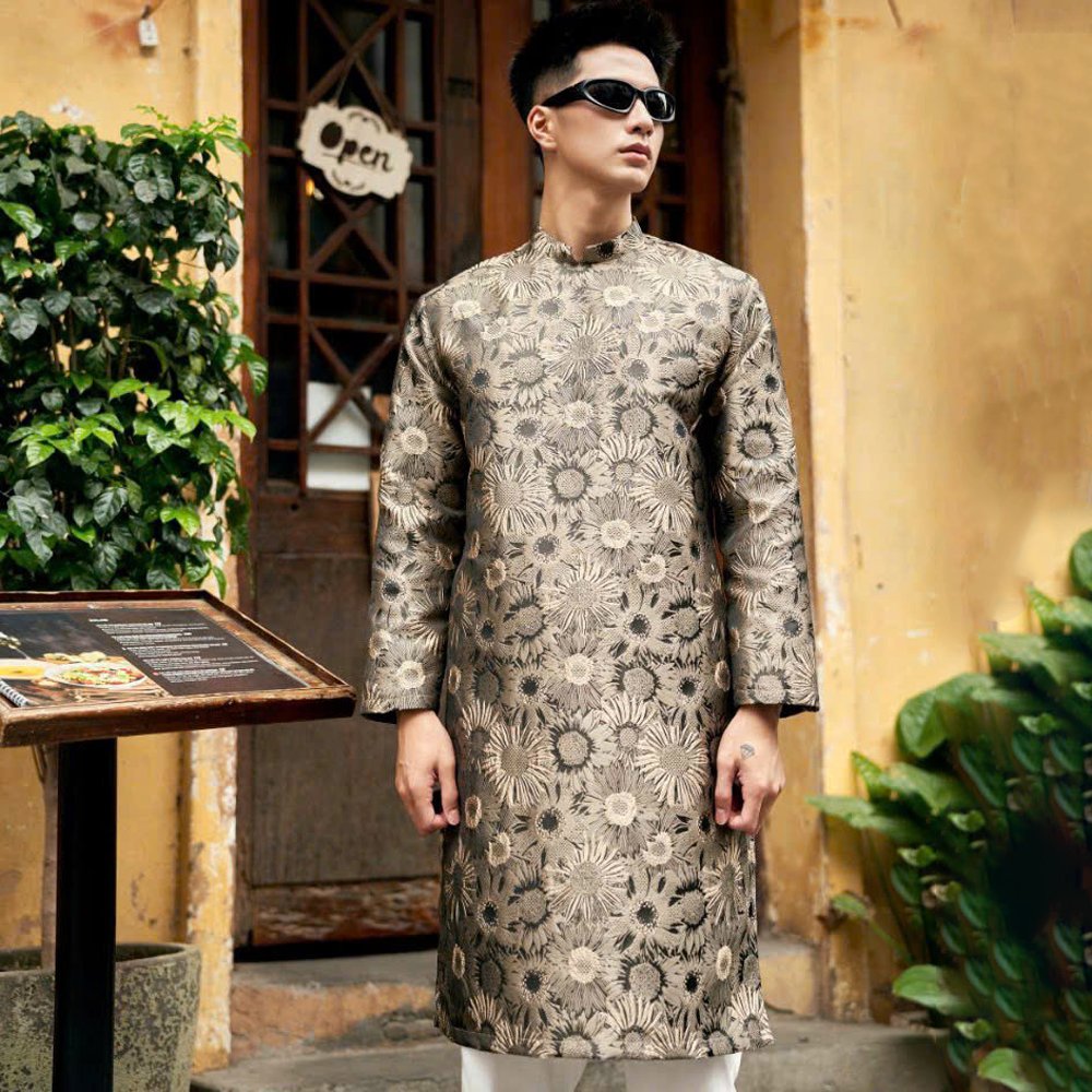 Thuê Áo Dài Nâu Gấm Nam Hoa Cúc Nổi tại Tiệm Nhà Bông – mẫu áo dài nam cách tân với họa tiết hoa cúc nổi tinh xảo, chất liệu gấm dày cao cấp, màu nâu trầm sang trọng, form chuẩn, size L. Phù hợp lễ Tết, chụp ảnh, cưới hỏi và sự kiện truyền thống.